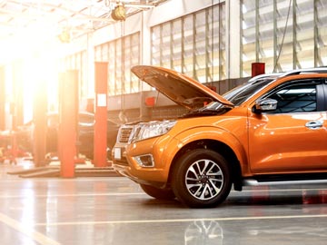 Ein orangefarbenes SUV steht in einer gut beleuchteten Auto-Werkstatt bei Autoankauf Fulda, dessen Motorhaube offen ist und den Motor zeigt.